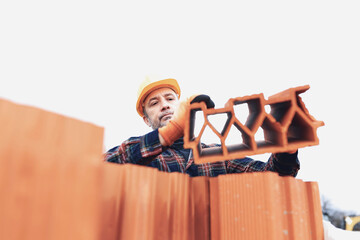 Bricklayer mason holding a regular brick outdoors on a construction site.