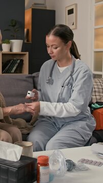 Vertical shot of millennial female medical specialist in uniform putting pulse oximeter on finger of elderly woman while carrying out home checkup