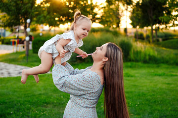 Obraz premium mom and child playing on a green lawn in the park in the summer, having fun together, mother and small child walking in the summer, playing on the grass
