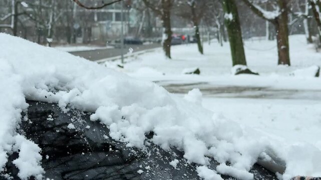 Detailed close up of gloved hand scraping thick snow and ice from frozen car windshield during snowfall. Winter driving safety and cold weather preparation concept in Slovakia.