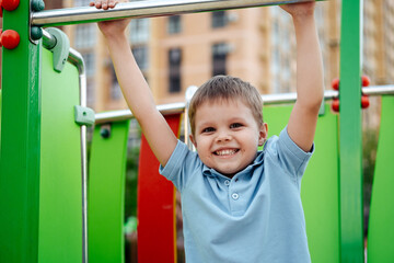 Fototapeta premium a child plays on a playground in the summer in the yard of a house, a smiling little boy enjoys the summer by playing on a playground