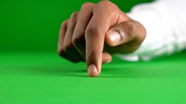 A person's index finger points down, touching a vibrant green surface, with a white sleeve visible.