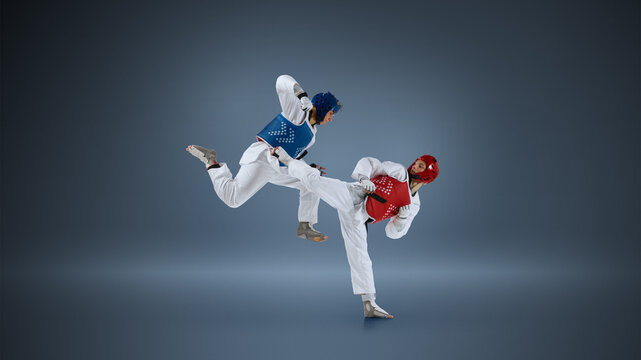 Taekwondo competitors executing high kick and counterattack in studio with red and blue body protectors. Concept of tactical combat strategy, professional martial arts duel and sport performance.