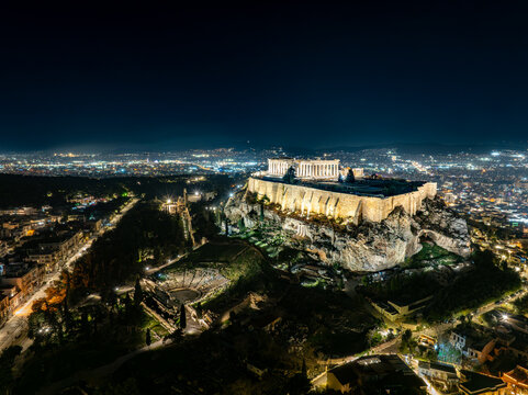 Aerial view of the illuminated Acropolis standing majestically atop a hill overlooking the sprawling, twinkling cityscape, a beacon of ancient history in the modern night, Athens, Greece.