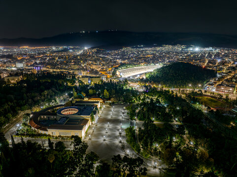 Aerial view of the illuminated Zappeion Hall and Panathenaic Stadium gleam amidst the dark tapestry of the city lights, Athens, Central Athens Regional Unit, Greece.