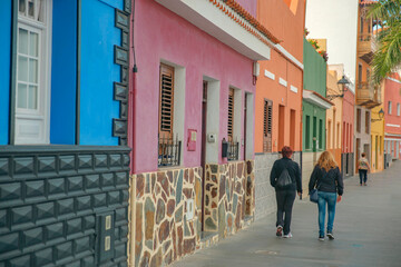 Fototapeta premium Tourists walking along colorful traditional houses on a street in Puerto de la Cruz with copy space