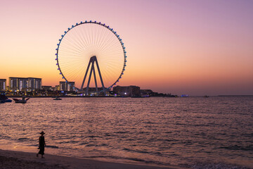 Sunset view of Bluewaters Island and Dubai Marina Ferris wheel from the beach, serene urban landscape, travel scene