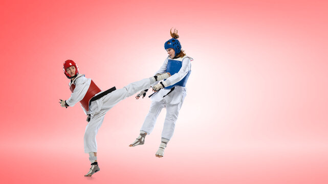 Female taekwondo athletes performing dynamic kick wearing red and blue protective gear on pink background. Concept of competitive sparring, women martial arts training and high intensity sport visuals