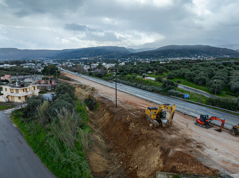 Aerial view of earth movers and construction equipment reshaping the landscape near the highway, against a backdrop of distant mountains, Chania, Chania, Greece.