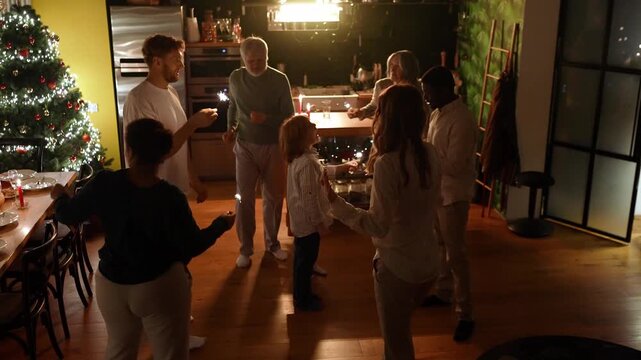 Grandson talking to male guest while family with guests dances and holds sparklers around them