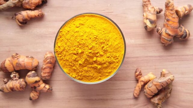 Top view of turmeric powder in a bowl with fresh roots on wooden background motion
