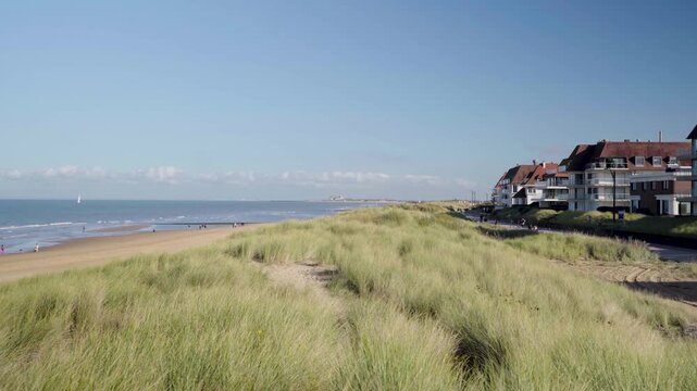 Pan from beach front houses over grass dune to knokke beach belgium