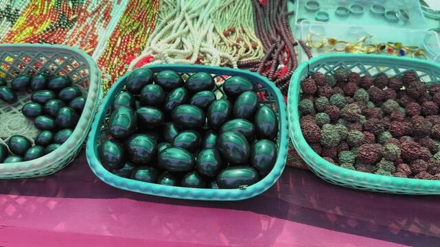 Close-up view of polished shivling stones and natural rudraksha beads arranged in plastic baskets at an outdoor market, showcasing texture, color, and handcrafted detail!!
