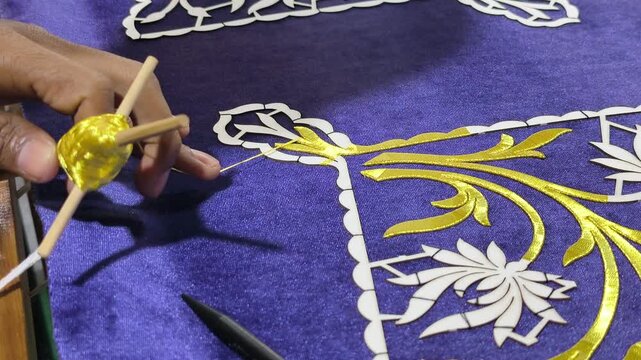 A skilled artisan performs traditional Malay Tekat embroidery. He meticulously sews gold thread onto rich velvet fabric. This rare, ancient craft represents a vanishing heritage art form.
