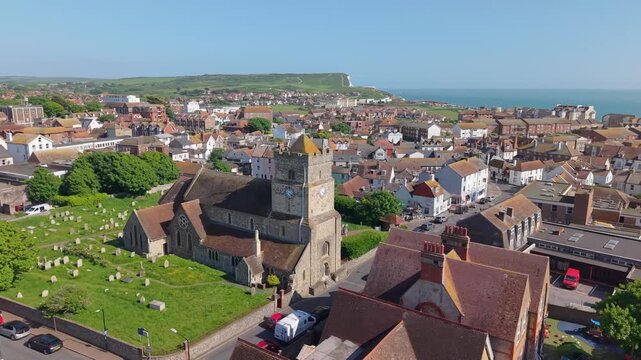 Drone orbit around St. Leonard's Church in Seaford, capturing the historic stone architecture, the surrounding green hills, and the stunning English Channel coastline.