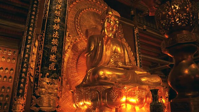 A majestic, large-scale golden Buddha statue seated on a lotus pedestal within the ornate wooden interior of the Bai Dinh Pagoda complex in Ninh Binh, Vietnam.