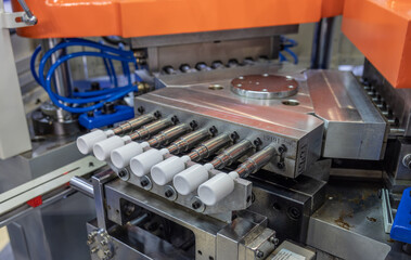 Close up of industrial plastic injection molding machine producing white plastic bottles in factory environment. Plastic packaging