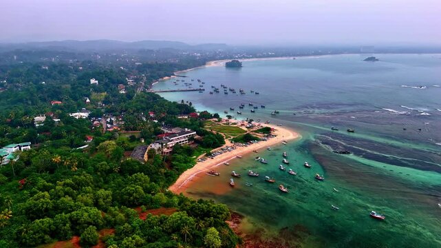 Aerial view of the fishing village and beach at Weligama, Sri Lanka, featuring a sandbar peninsula, turquoise waters and lush green surroundings.