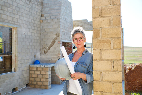 Confident home owner and architect at construction site with blueprint