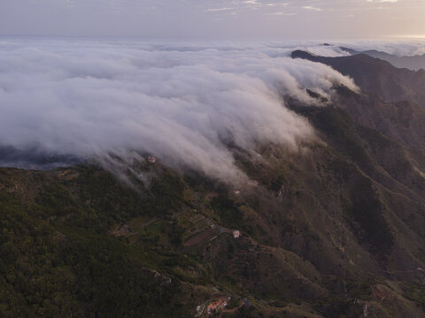 Aerial view of the clouds rolling over the rugged, mountainous terrain, creating a soft, ethereal blanket over the landscape, Anaga, Canarias, Spain.
