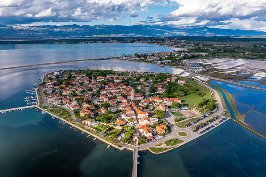 Aerial view of the historic old town, with its terracotta rooftops, surrounded by the shimmering Adriatic Sea and distant mountains, Nin, Zadar County, Croatia.