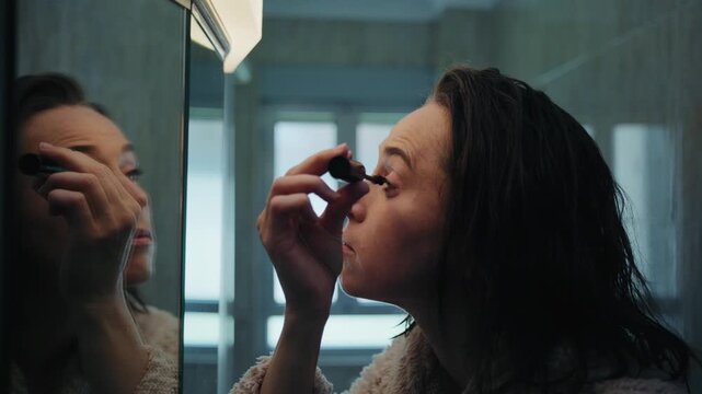 Woman Applying Mascara to Eyelashes in a Bathroom Mirror