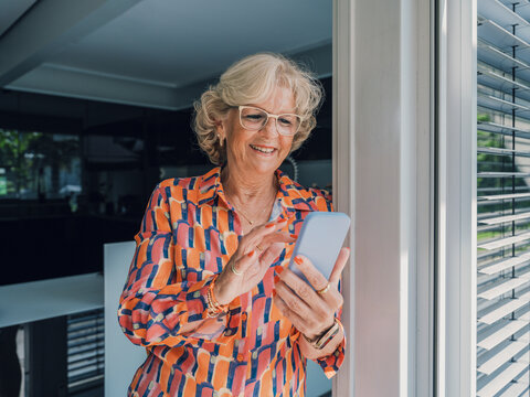 Woman in colorful dress using smartphone at home near doorframe