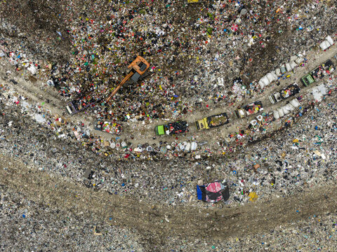 Aerial view of a sprawling landfill where trucks navigate a path through the waste, contrasting the stark reality of waste management, Denpasar, Bali, Indonesia.
