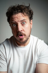 Fototapeta premium Man with Curly Hair and Beard Looking at the Camera with a Surprised Expression and Open Mouth