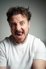 Fototapeta premium Close-up of a Man with Curly Hair and Beard Making an Intense Shouting Face with Tongue Visible