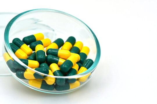 Green and Yellow Tramadol Capsule Pills in Glass Bowl on White Background with copy space.