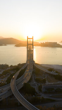 Aerial view of the Tsing Ma Bridge elegantly spans the water under a golden sun, its steel cables contrasting with the soft sunset, Hong Kong, Hong Kong.