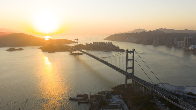 Aerial view of the Tsing Ma Bridge stretching across the water, bathed in the warm glow of the setting sun, Hong Kong, Hong Kong.