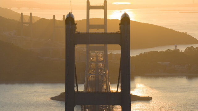 Aerial view of Tsing Ma Bridge bathed in the warm glow of the setting sun, its colossal structure piercing the horizon, Hong Kong, Hong Kong.
