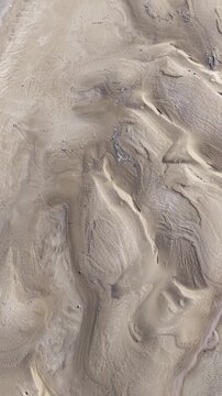 Top-down aerial view of a solitary lighthouse on a sandy beach with natural patterns