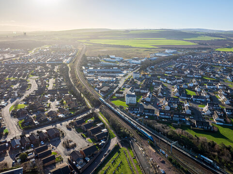 Aerial view of a train slicing through the heart of the town, dividing rows of houses from the distant green fields, Dunbar, Scotland, United Kingdom.
