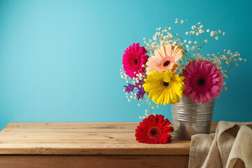 Gerbera daisy flower bouquet in bucket on wooden table over blue background. Spring and Easter holiday concept
