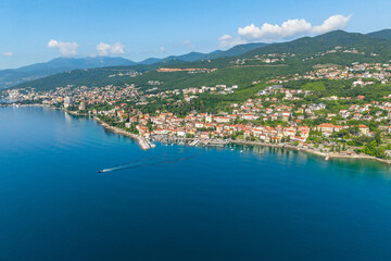 Obraz premium Aerial view of coastal town Volosko, Opatijska riviera, Croatia, with red rooftops along blue Adriatic Sea and green hills. Scenic Mediterranean landscape with marina and boat trail on calm water