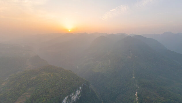 Aerial view of the sun kisses the peaks of the misty mountains, its golden light filtering through the valleys, Glassbridge, Zhangjiajie, China.