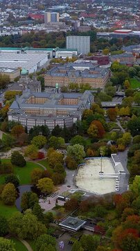 4K aerial vertical video of Planten un Blomen park in Hamburg. Aerial view of EisArena rink, autumn foliage, and exhibition halls. Vertical video for Germany travel reels.