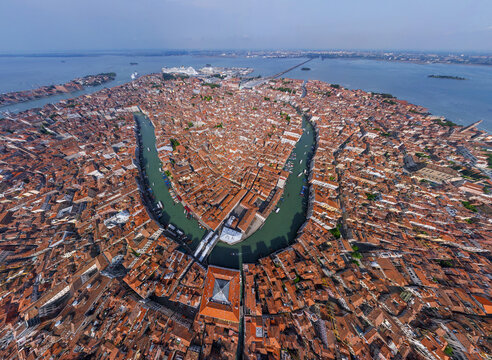 Aerial view of terracotta rooftops cascade down to meet winding canals, reflecting the sky's soft light, creating a mesmerizing blend of urban density and serene waterways, Venice, Veneto, Italy.