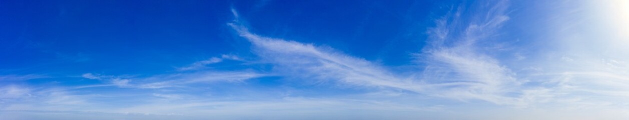 Wide panoramic landscape of clear blue sky with flowing cloud patterns stretching across frame, captured in natural daylight to express calm atmosphere, simplicity, and minimal background aesthetic.