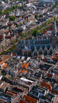 4K aerial vertical video of Amsterdam city center and Oude Kerk. Aerial view of historic canal houses, waterways, and De Wallen district. Vertical video for Netherlands travel reels.