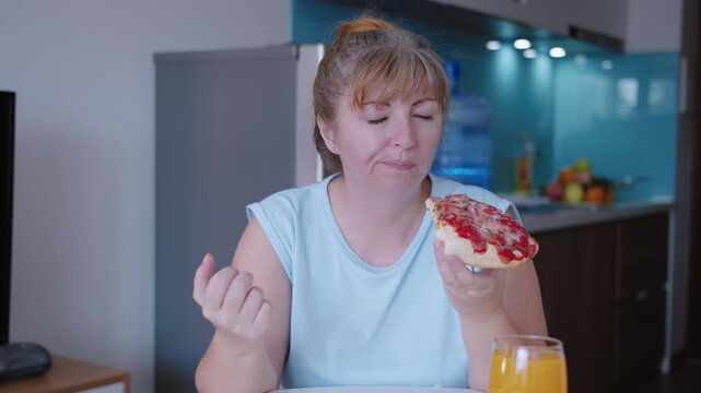 Woman eats a slice of pizza with gusto, takes it out of the box and eats it, sitting at the kitchen