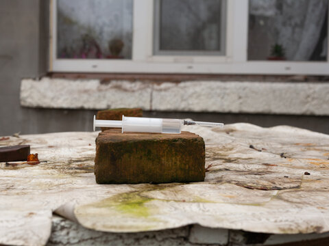 An unused plastic syringe lies on a brick in the street.