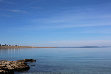 Scenic rocky coastline of Pag Island in Croatia with calm Adriatic Sea under a clear blue sky. Coastal town visible in the distance with mountains on the horizon. Natural Mediterranean landscape