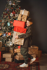 Boy carries gifts beside a Christmas tree with decorations and lights