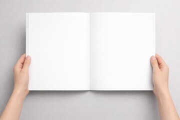 Fototapeta premium Hands holding an open blank book on a gray background viewed from above