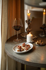 Obraz premium Elegant bresaola appetizer with honey ricotta on skewers served on white plate and red wine in candlelit fine dining setting