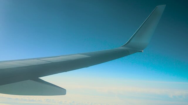 Plane flying above clouds with visible wingtip and flaps. Jet cruising high with aerodynamic wing structure in view. Airliner gliding over sky layers showing winglet and surface panels